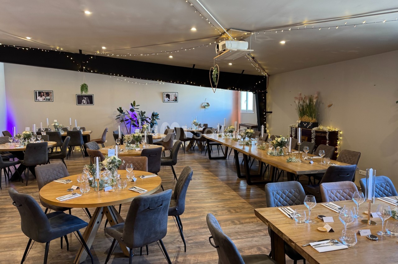 Salle de réception décorée avec des tables rondes et rectangulaires, ornées de fleurs et de bougies, éclairage chaleureux.