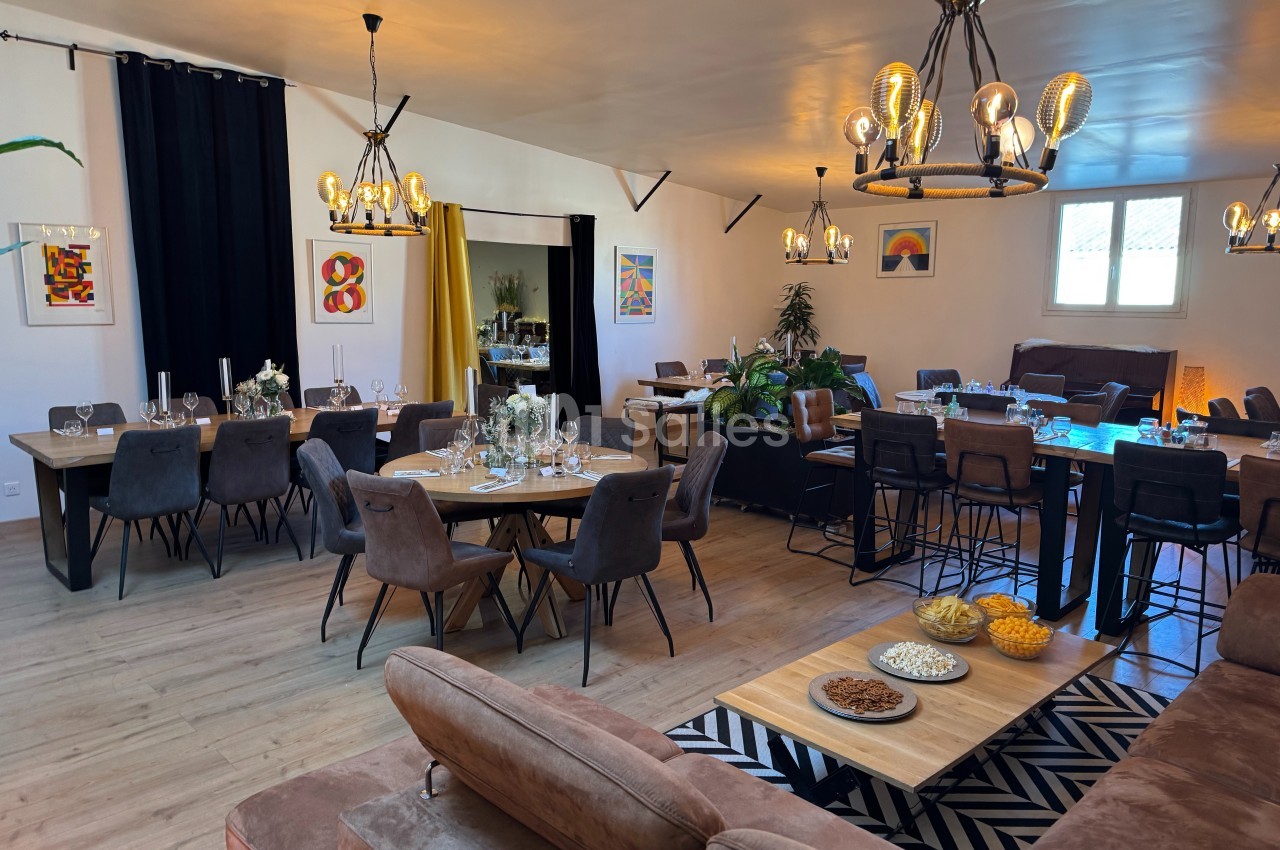 Salle lumineuse aménagée avec des tables dressées, des chaises modernes, des décorations murales et des luminaires suspendus.