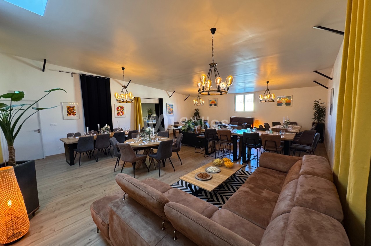 Salle lumineuse avec canapés, grandes tables dressées, suspensions décoratives et plantes en arrière-plan.