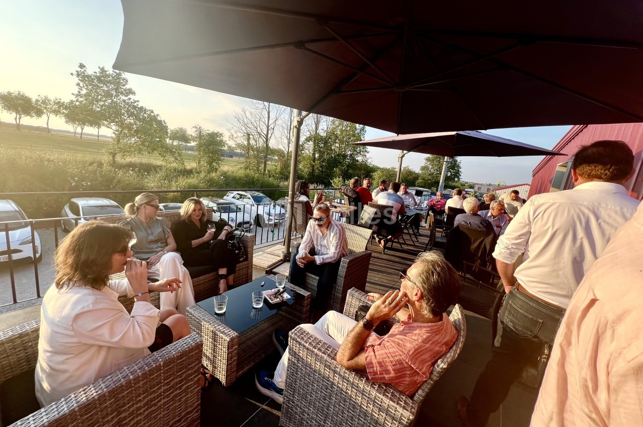 Personnes assises en terrasse, discutant et partageant un moment convivial sous des parasols au coucher du soleil.