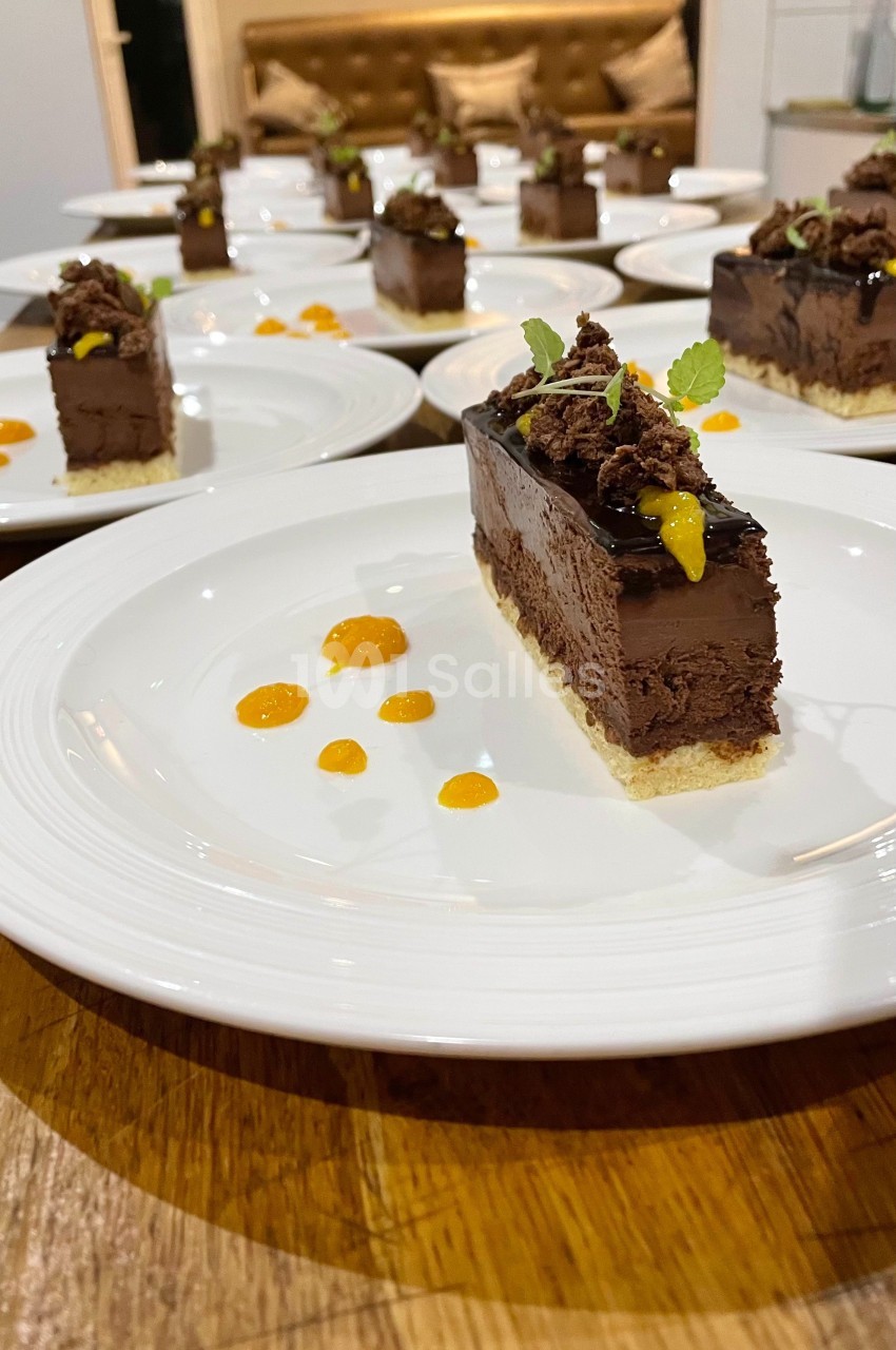 Part de gâteau au chocolat décorée de feuilles de menthe et de coulis orange, servie sur une assiette blanche.