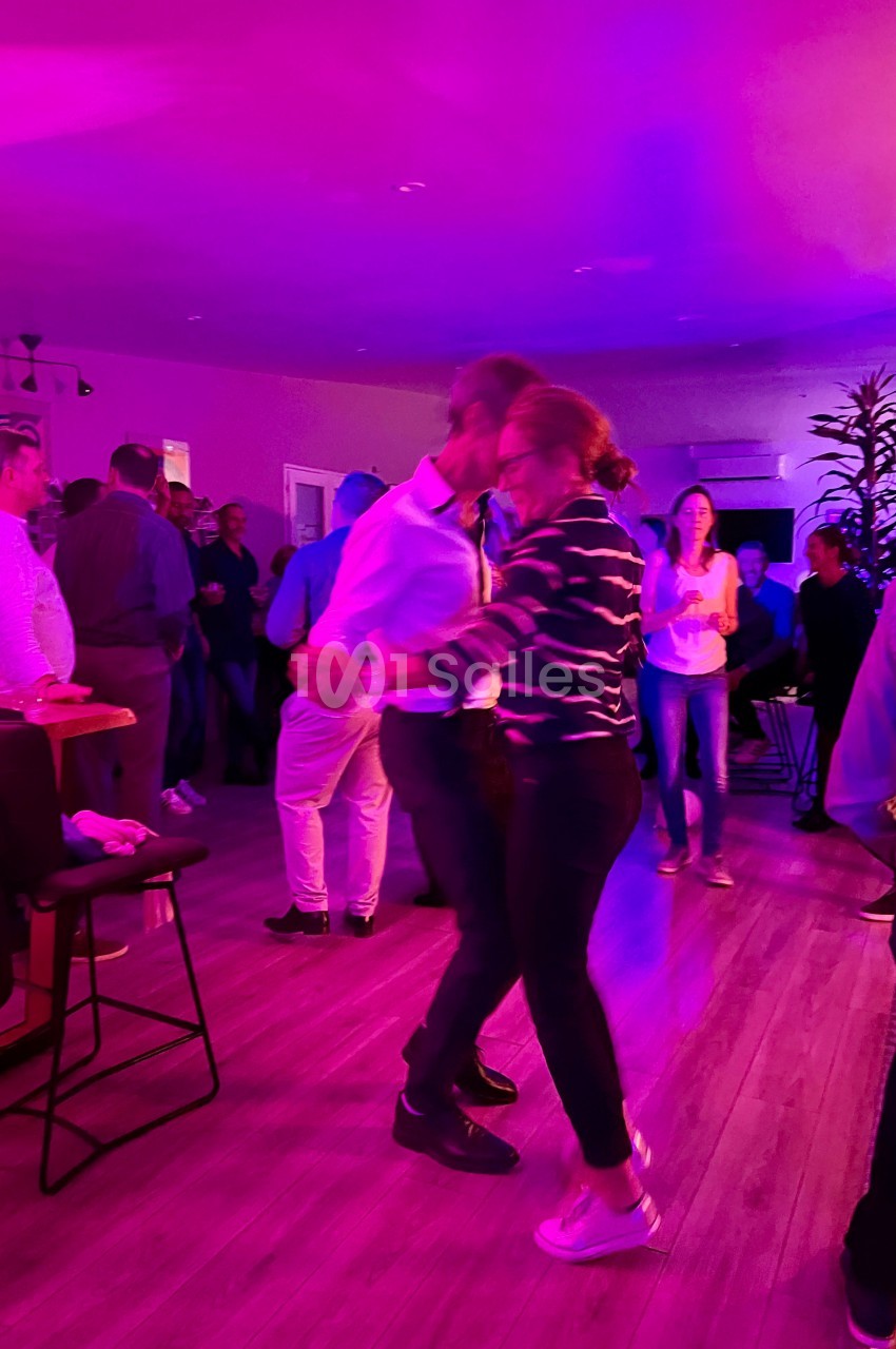 Deux personnes dansent dans une salle éclairée par des lumières colorées, entourées de spectateurs.