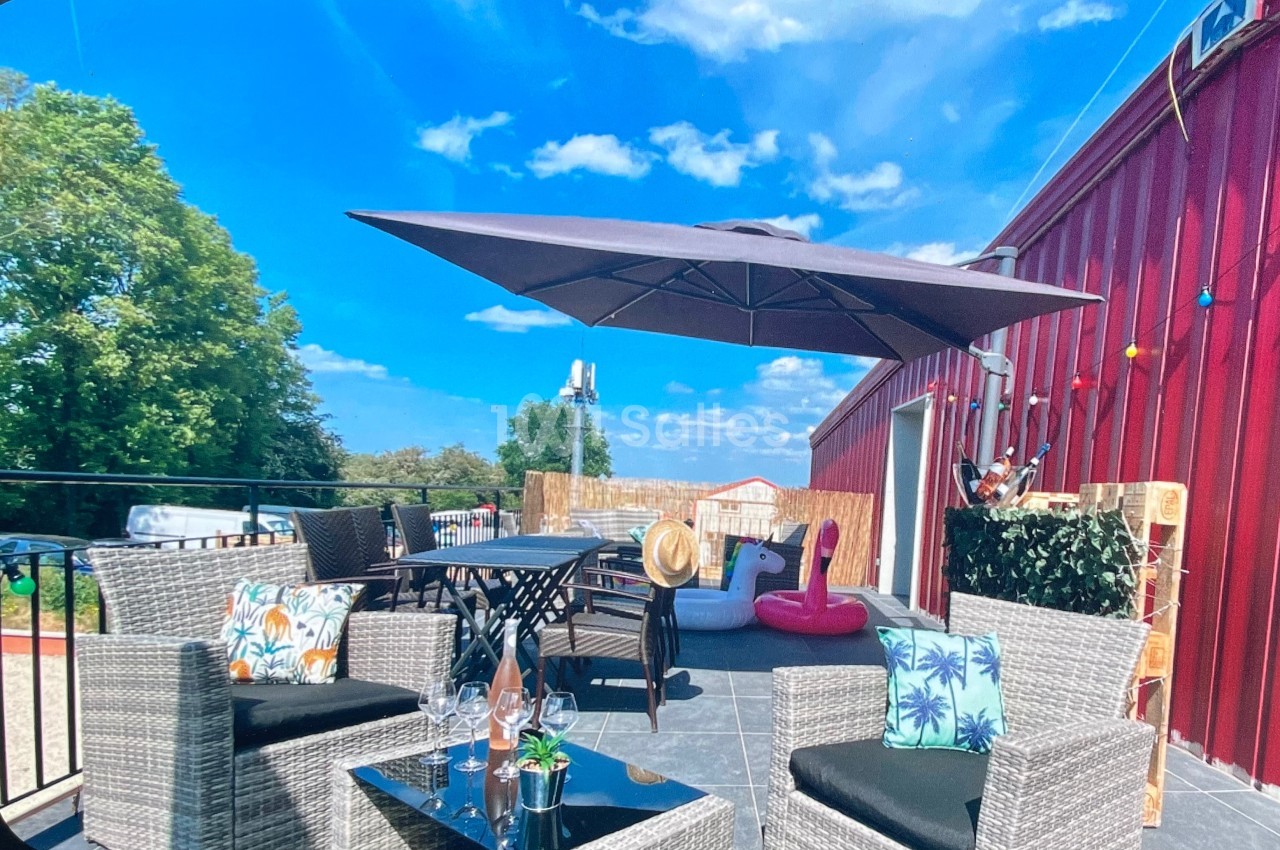 Terrasse ensoleillée avec mobilier en rotin, parasol, table, chaises, et décoration estivale, vue sur un ciel bleu.