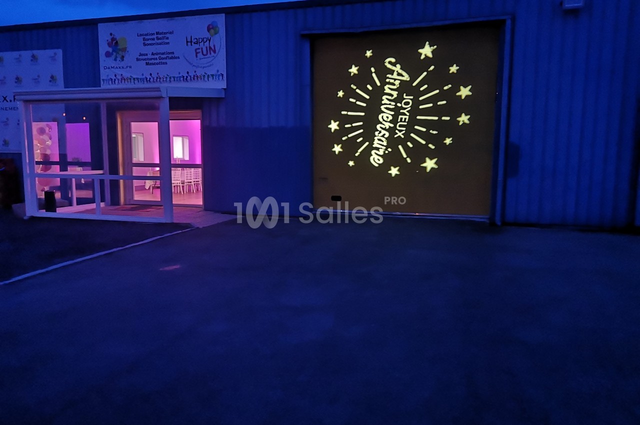 Façade d'un bâtiment éclairé avec une projection lumineuse ’Joyeux Anniversaire’ et des étoiles sur un mur.