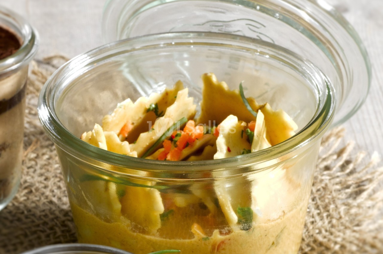 Raviolis disposés dans un bocal en verre avec une sauce crémeuse et des herbes fraîches.