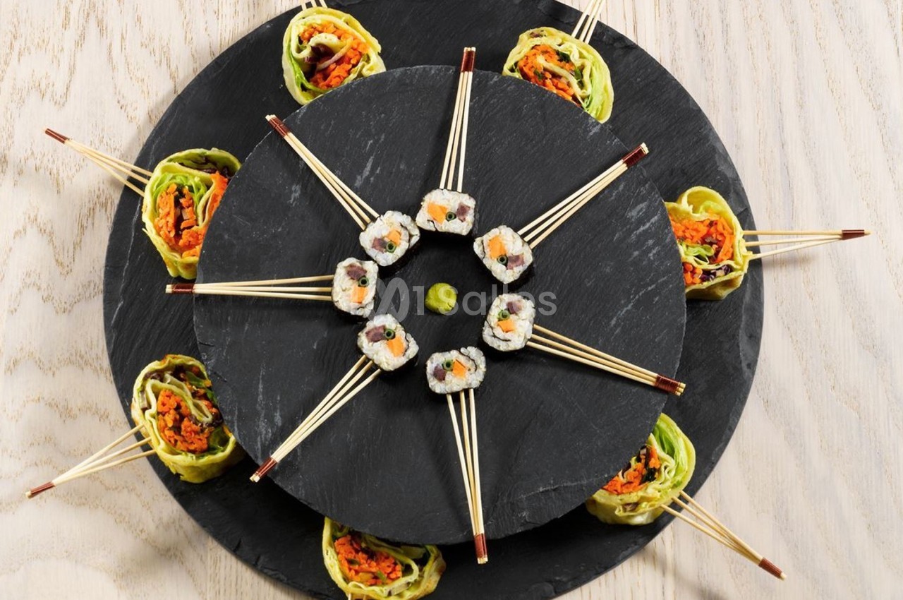 Assortiment de sushis et rouleaux de légumes disposés en cercle sur des plateaux en ardoise avec des baguettes.