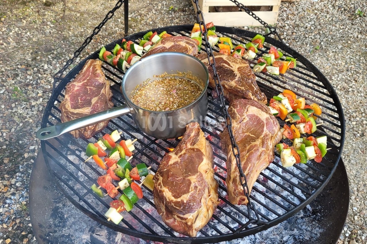 Viandes grillées et brochettes de légumes colorés cuisant sur un barbecue rond avec une casserole au centre.