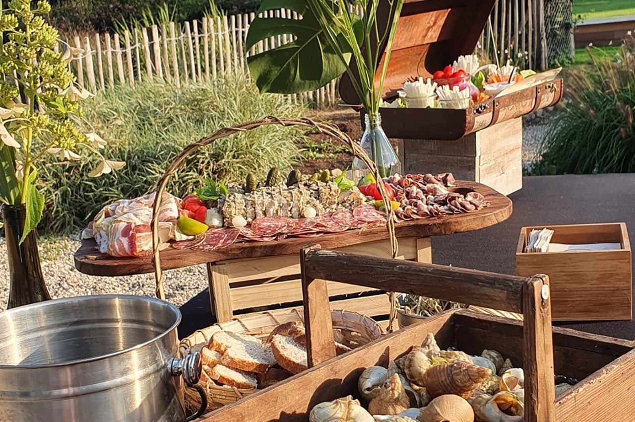 Plateau de charcuterie, fruits de mer et pain disposés sur des tables en bois dans un cadre extérieur verdoyant.