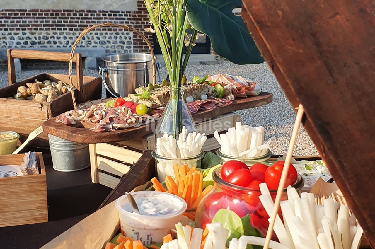 Plateau de légumes croquants, dips et charcuterie disposés sur une table en extérieur, avec des décorations végétales.