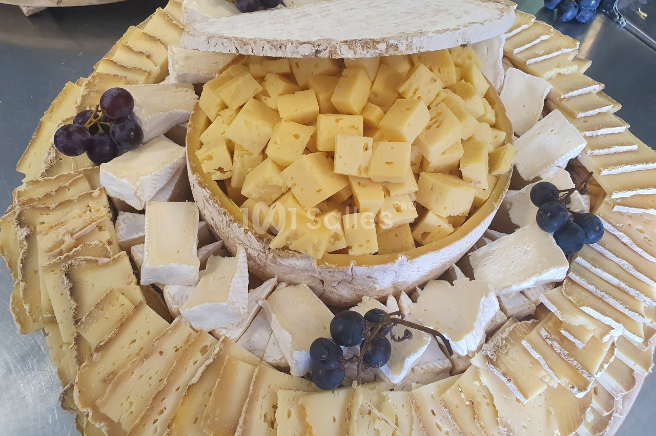 Plateau de fromages variés avec morceaux de fromage à pâte dure au centre, entourés de tranches et de raisins noirs.