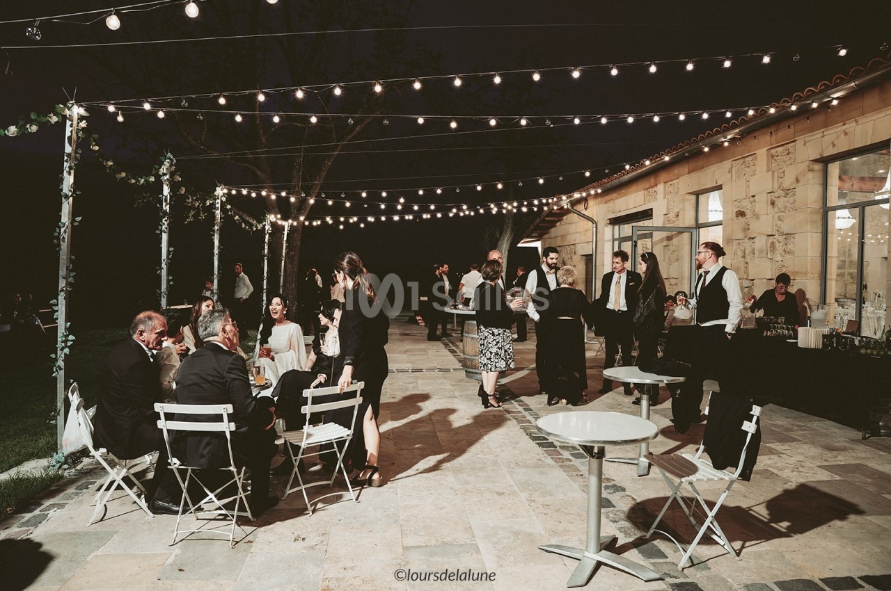 Personnes discutant et partageant un repas en soirée sur une terrasse éclairée par des guirlandes lumineuses.