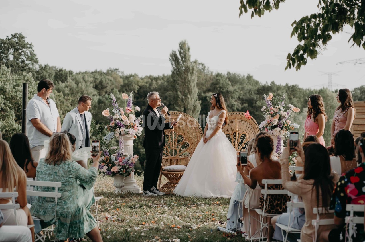Cérémonie de mariage en plein air avec un officiant s'adressant à la mariée devant des invités assis.