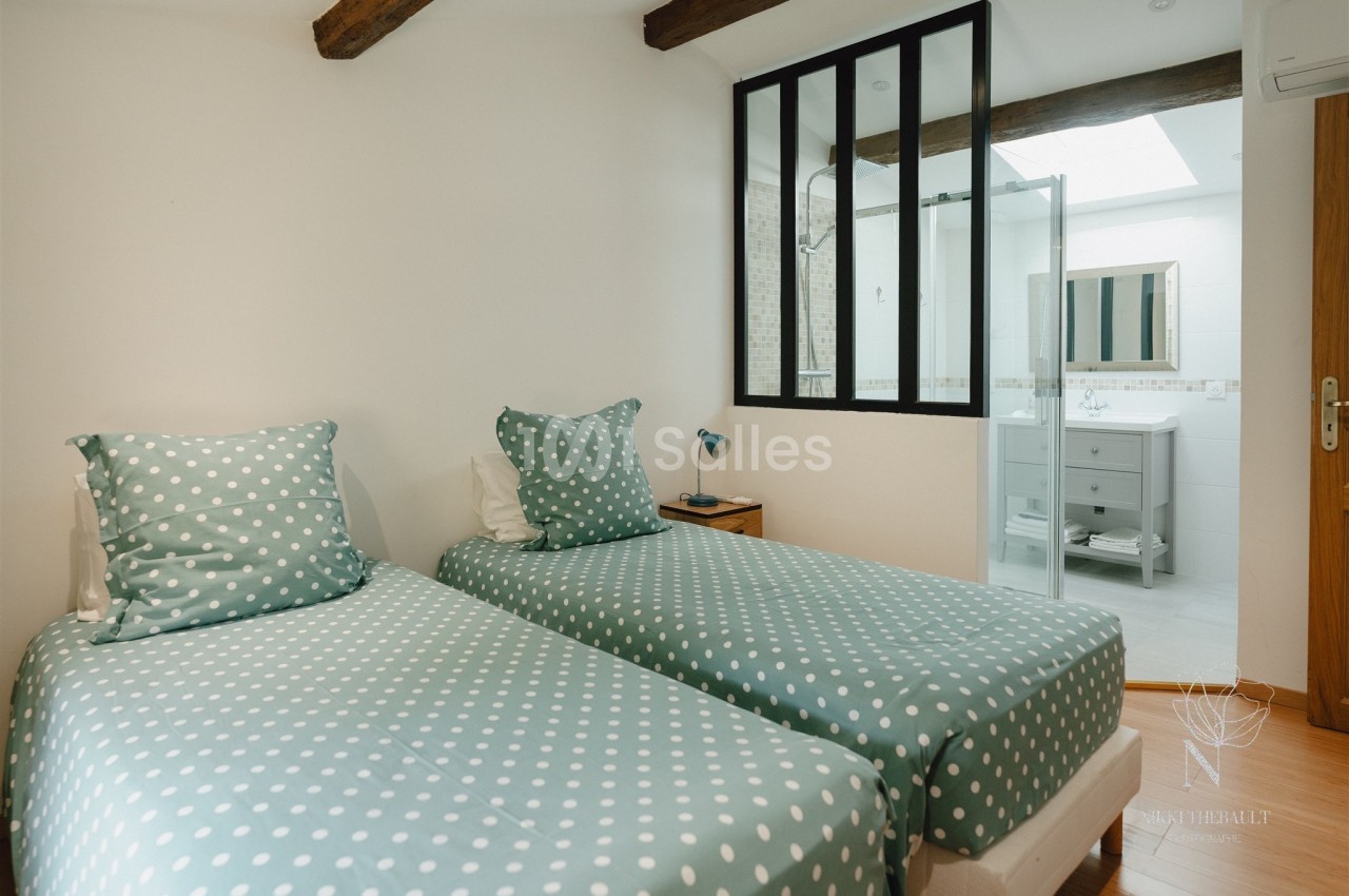 Deux lits simples avec housses à pois verts dans une chambre lumineuse, vue sur une salle de bain attenante.
