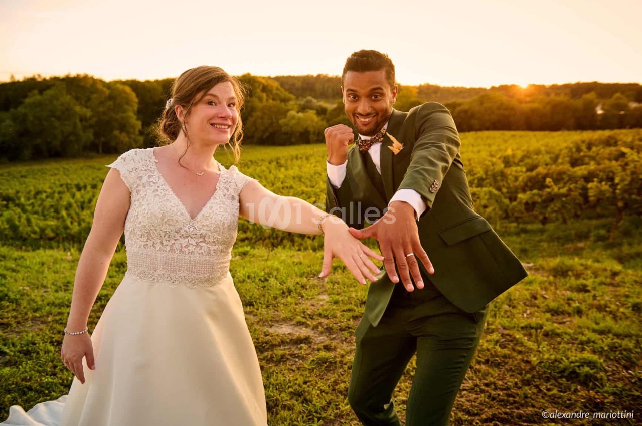 Un couple en tenue de mariage montre leurs alliances dans un champ au coucher du soleil.