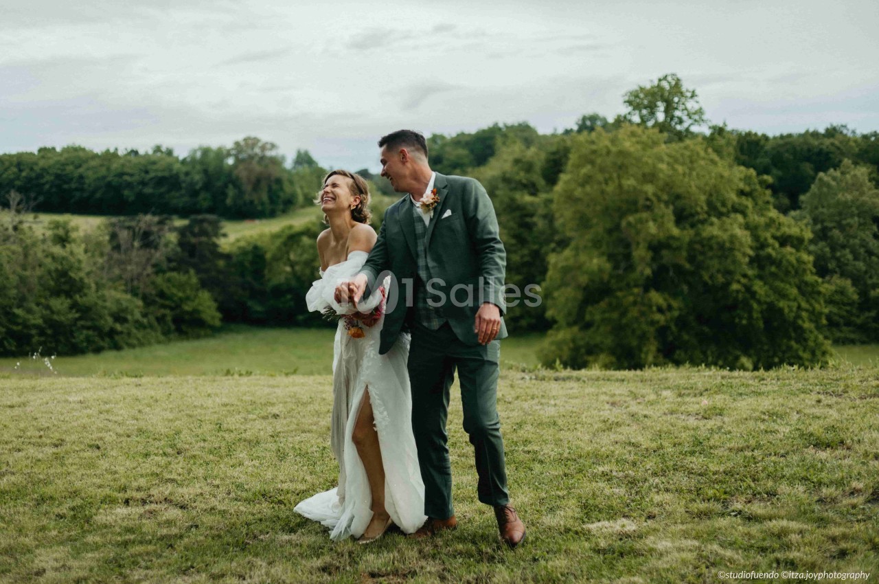 Un couple souriant marche dans un champ verdoyant sous un ciel nuageux.