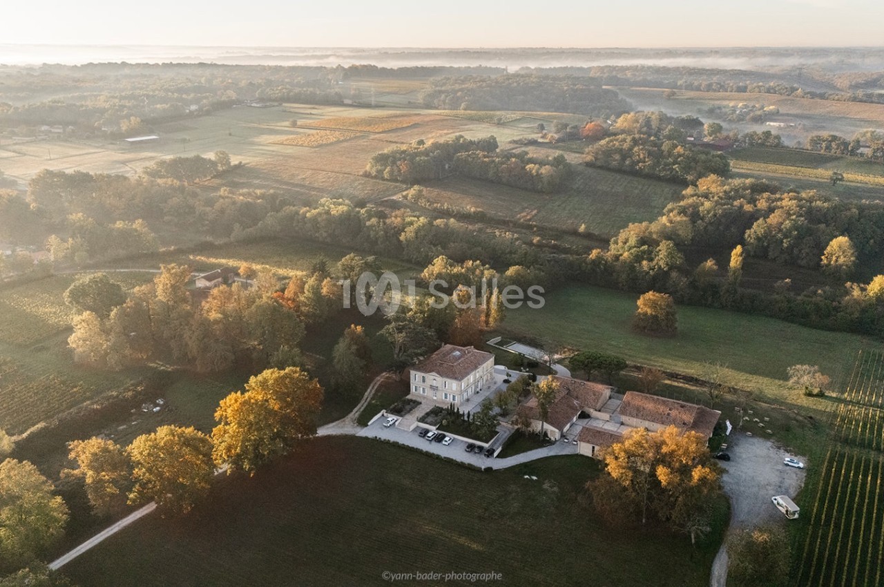 Vue aérienne d'une propriété entourée de champs, de vignes et de forêts sous une lumière douce du matin.