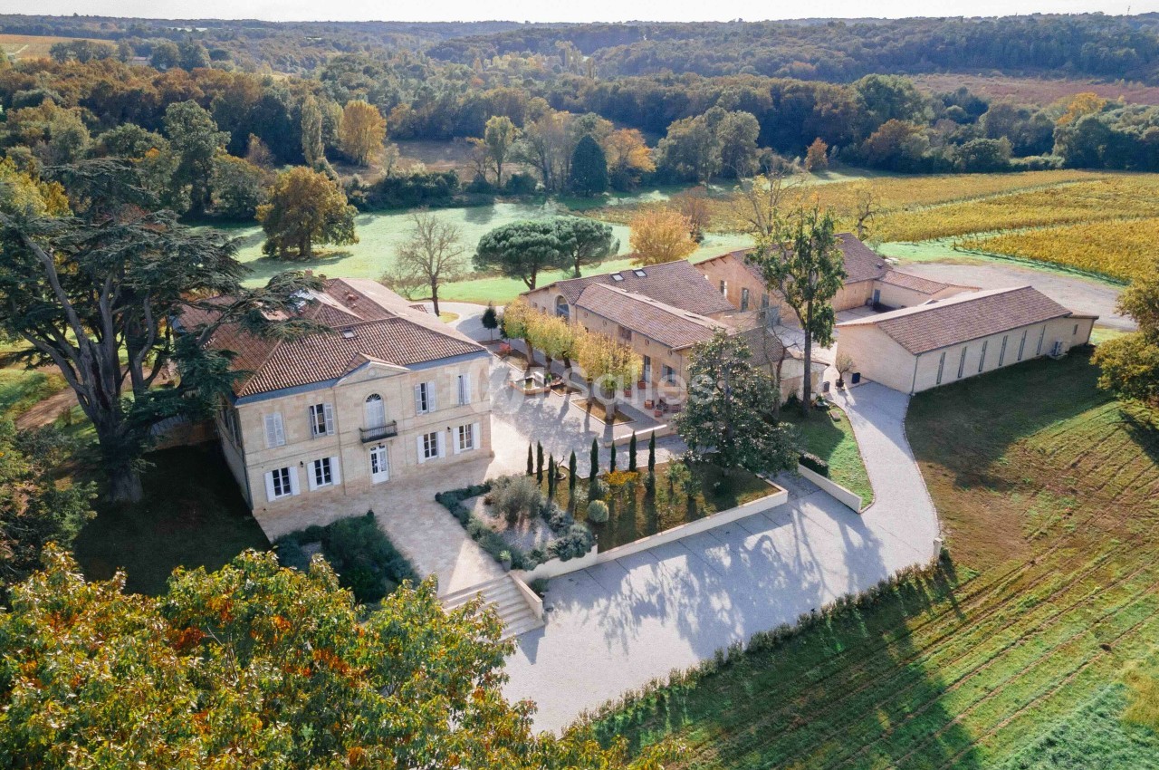 Vue aérienne d'un domaine avec bâtiments en pierre, cour centrale, jardins et vignes environnantes.