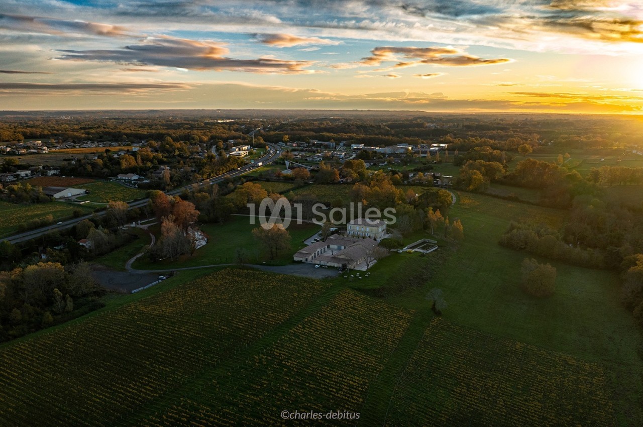 Vue aérienne d'une campagne au coucher du soleil, avec un grand bâtiment entouré de champs et de végétation.