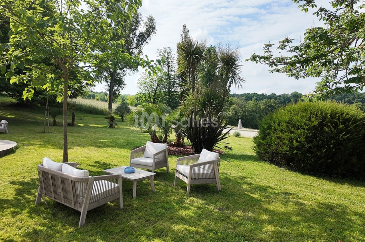 Mobilier de jardin en bois avec coussins blancs disposé sur une pelouse entourée d'arbres et de végétation.