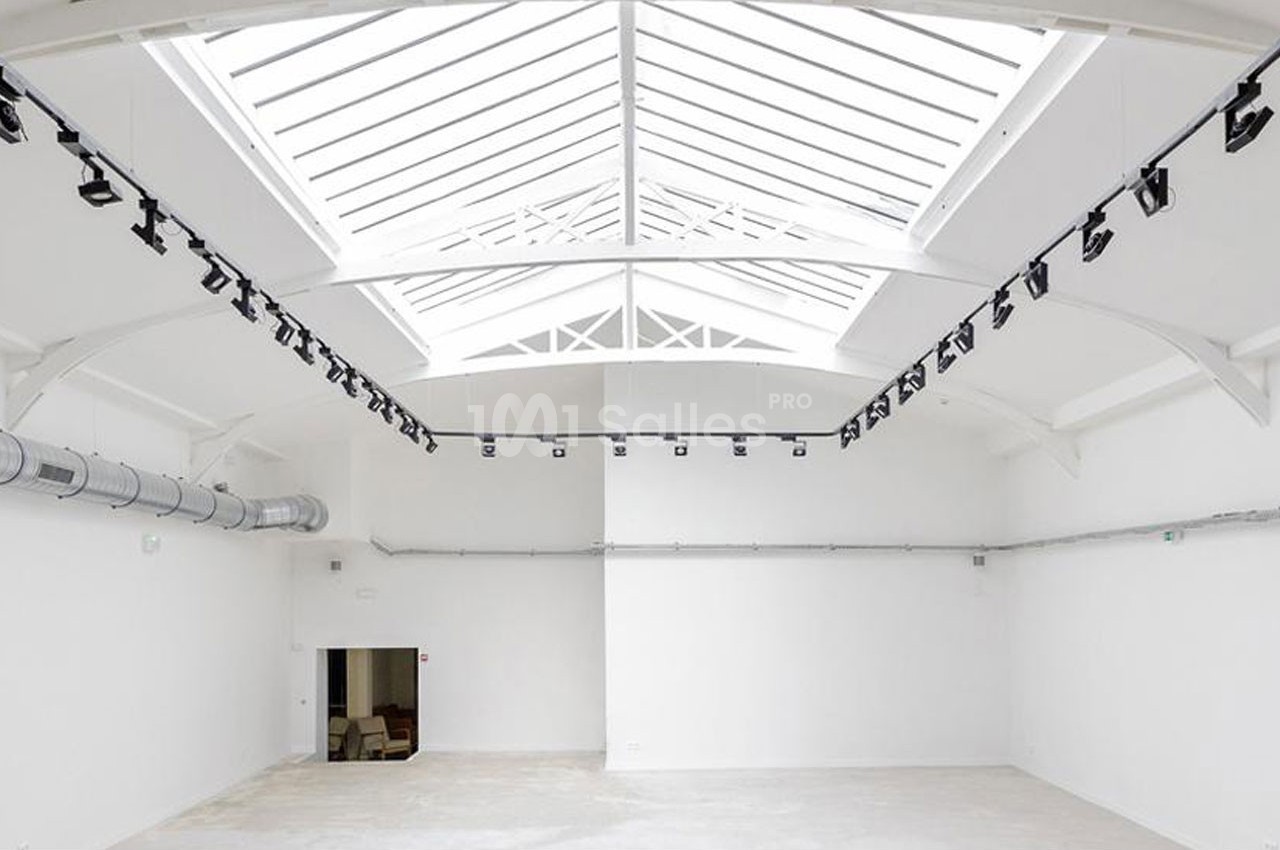 Vue intérieure d'un espace vide avec un plafond en verrière, des murs blancs et un éclairage suspendu.