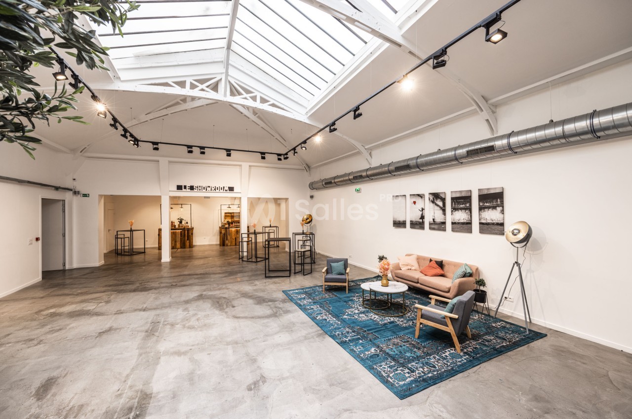 Salle lumineuse avec verrière, mobilier moderne, canapé, tapis bleu et décorations minimalistes.