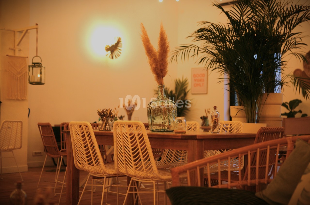 Salle à manger chaleureuse avec table en bois, chaises en rotin, vase décoratif et plantes en arrière-plan.