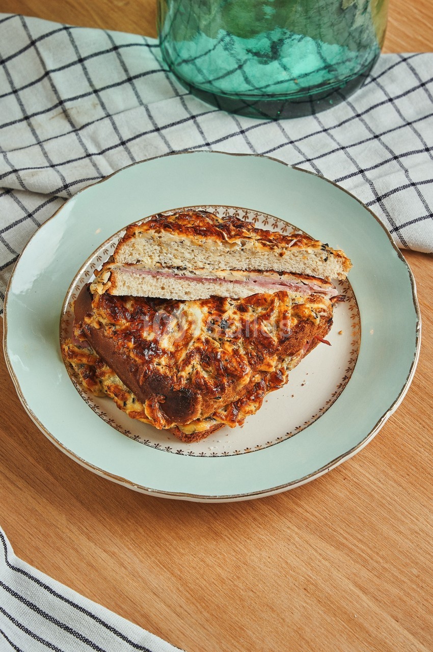 Croque-monsieur doré et gratiné, coupé en deux, servi sur une assiette blanche bordée de motifs.