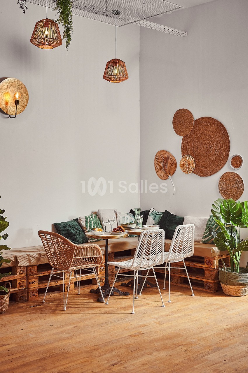 Coin salon chaleureux avec table en bois, chaises en rotin, coussins verts, plantes et décorations murales en osier.