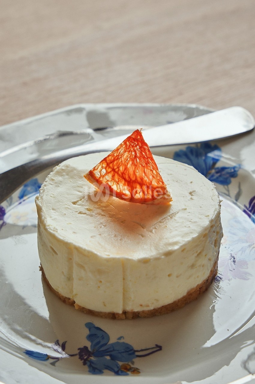 Gâteau au fromage individuel sur une assiette fleurie, garni d'un segment d'orange sanguine.