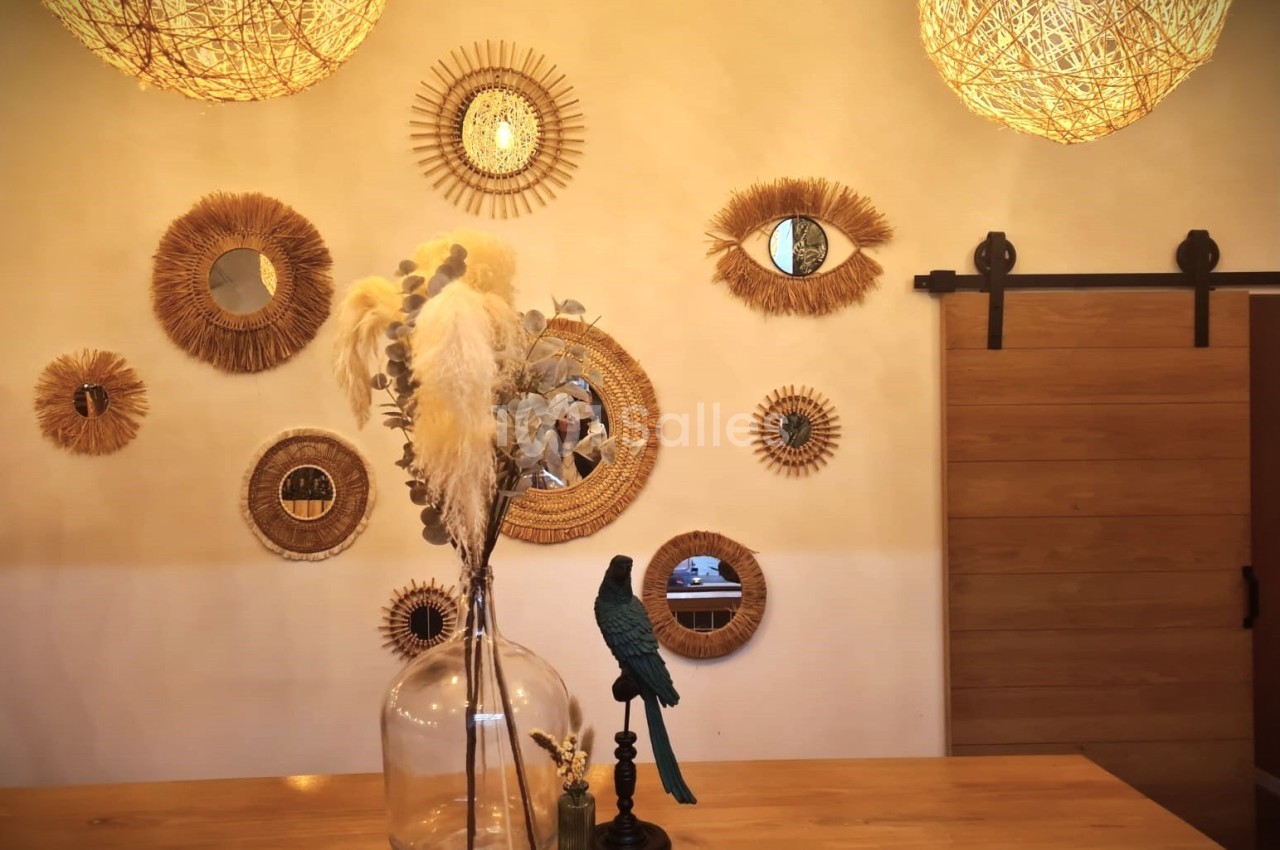Décoration murale avec miroirs ronds et en forme d'œil, vase avec plantes séchées et statuette d'oiseau sur une table.