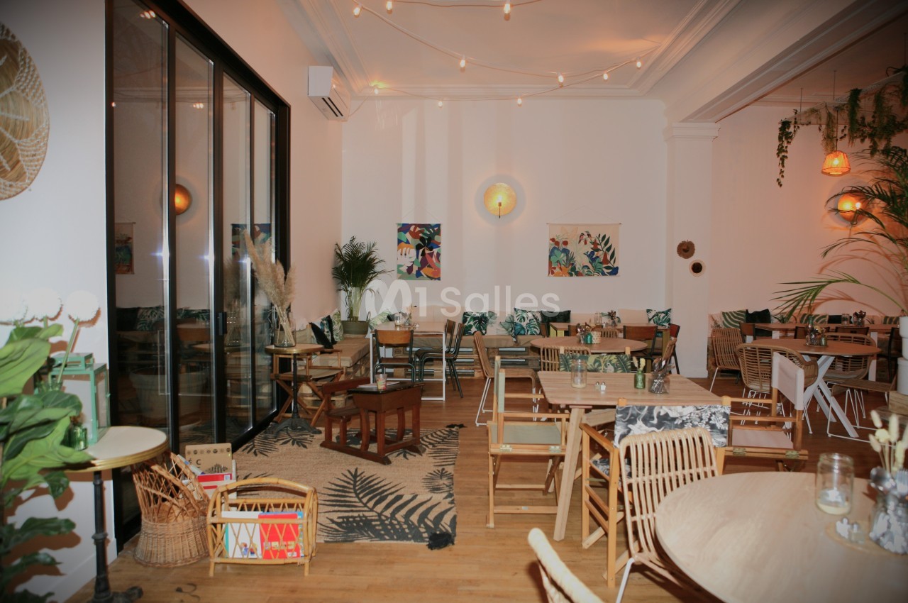 Salle lumineuse avec décoration tropicale, mobilier en bois, plantes vertes et guirlandes lumineuses suspendues.