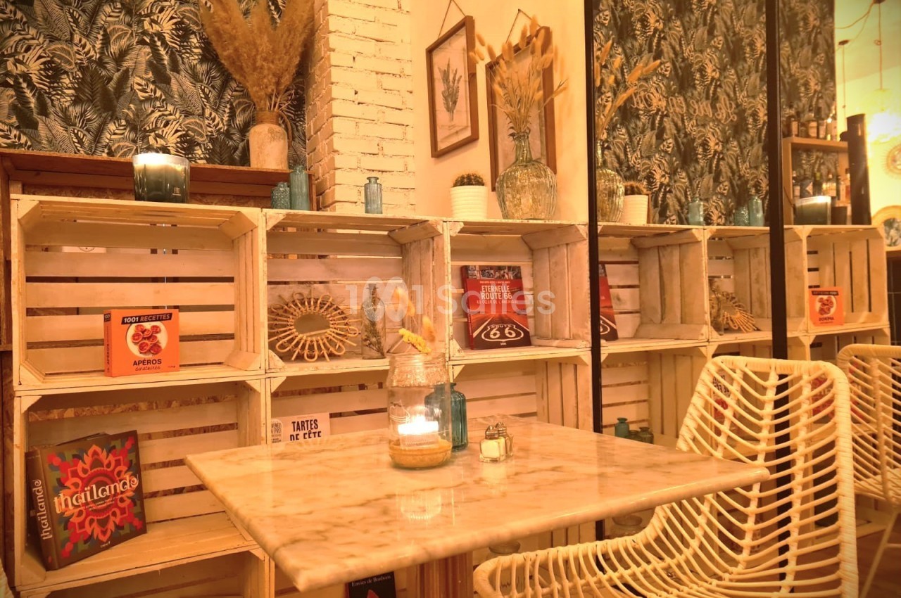 Table en marbre entourée de chaises en rotin, devant des étagères en caisses de bois décorées de livres et objets.