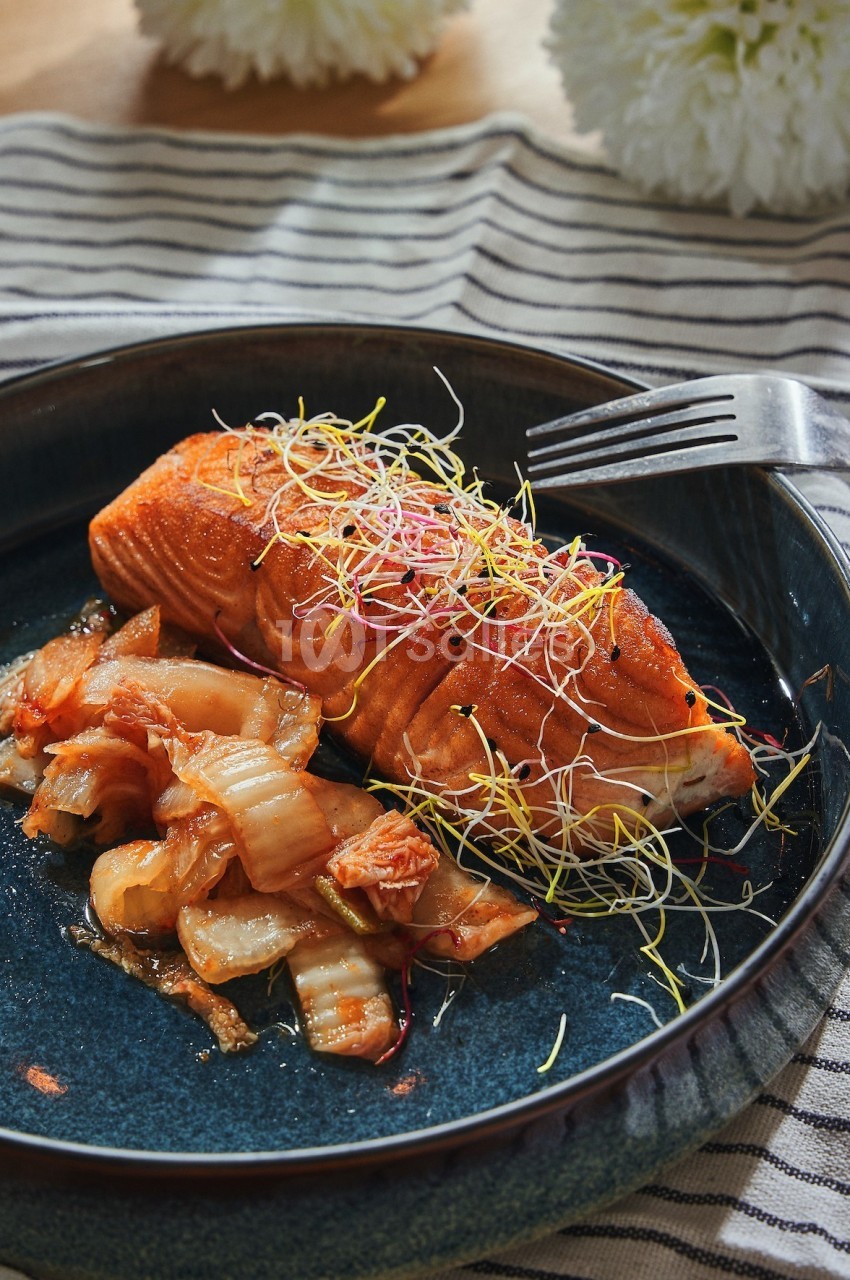 Filet de saumon grillé garni de pousses, accompagné de légumes sautés, servi dans une assiette en céramique bleue.