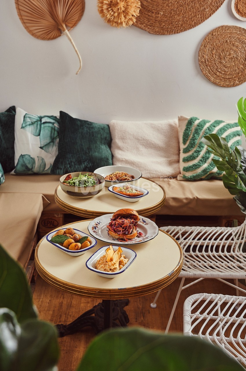 Assiettes de plats variés disposées sur des tables rondes dans un salon décoré de coussins et d'éléments naturels.