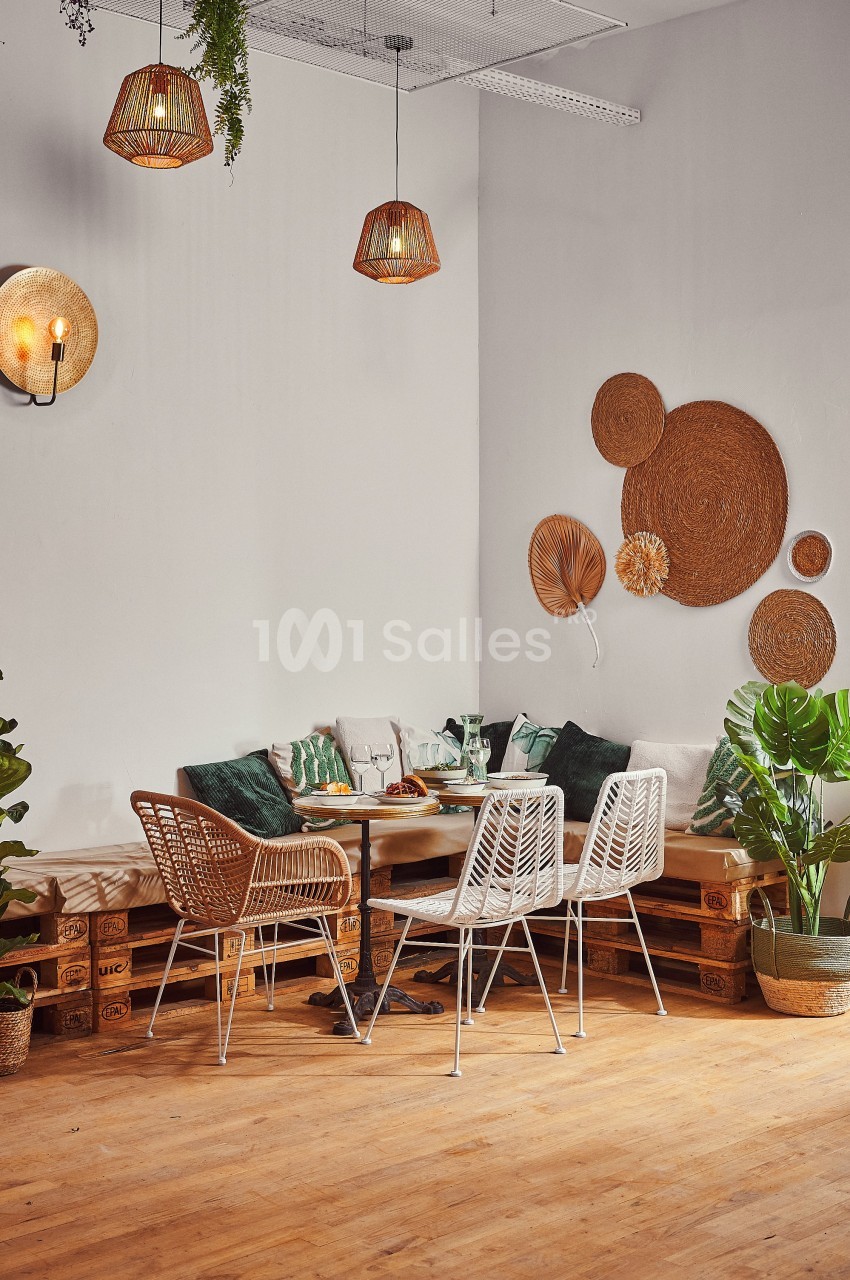 Coin repas cosy avec table en bois, chaises en rotin, coussins verts, plantes et décorations murales en osier.