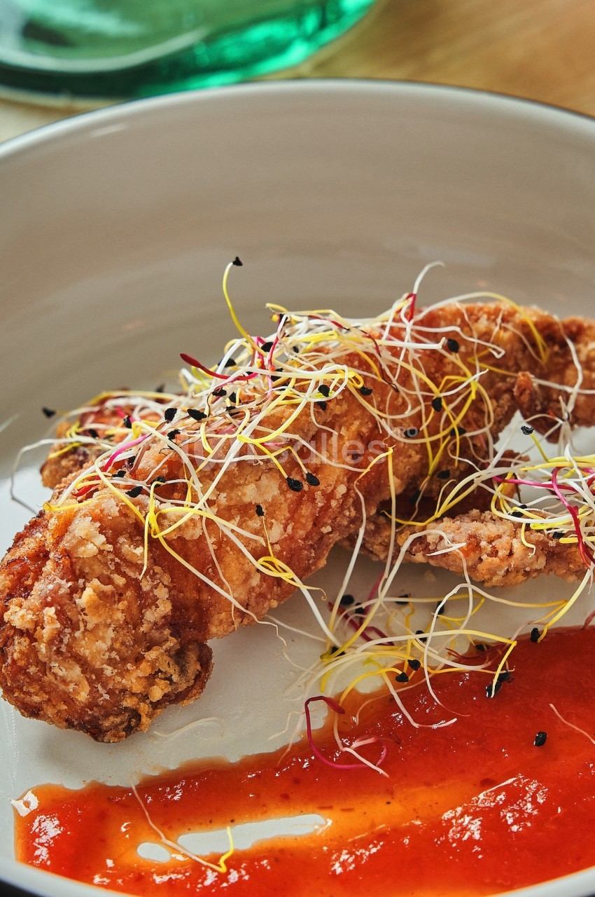 Plat de crevette panée garnie de pousses colorées, accompagné d'une sauce rouge servie dans une assiette blanche.