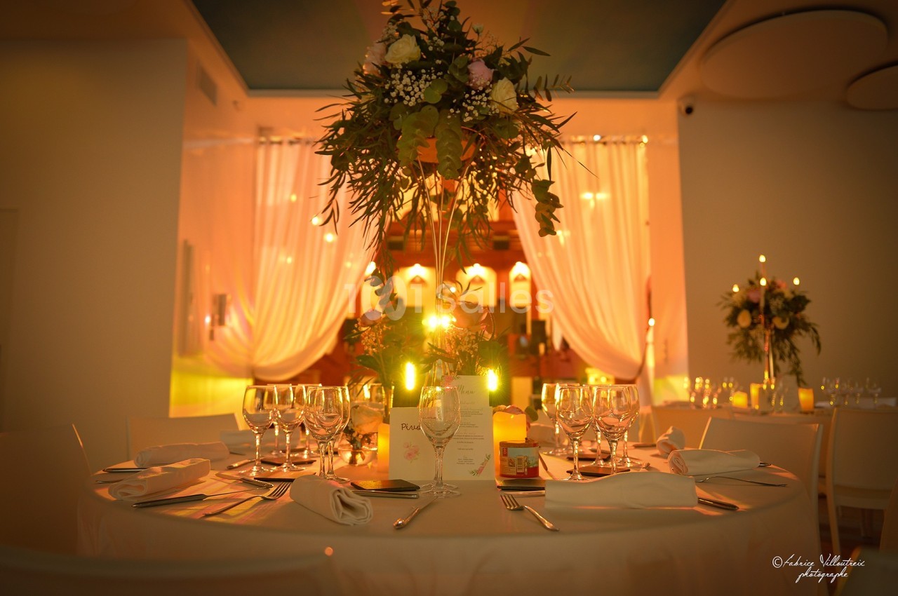 Table élégamment dressée avec des verres, des assiettes et un centre de table floral, éclairée par une lumière chaleureuse.