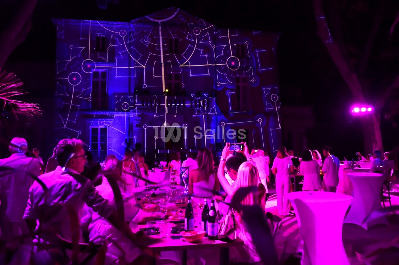Des invités profitent d'une soirée en plein air avec des projections lumineuses sur la façade d'un bâtiment.
