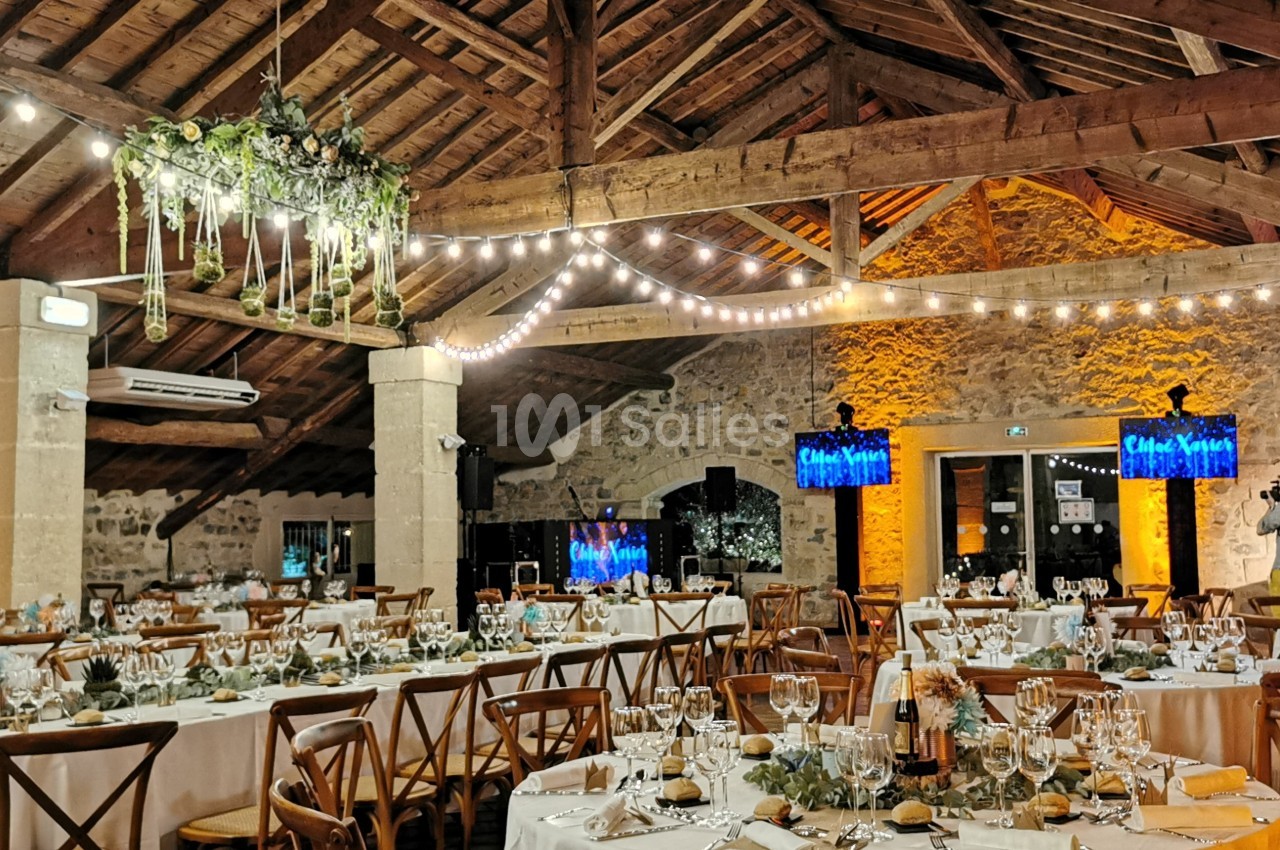 Salle de réception avec tables dressées, chaises en bois, guirlandes lumineuses et décoration végétale suspendue.