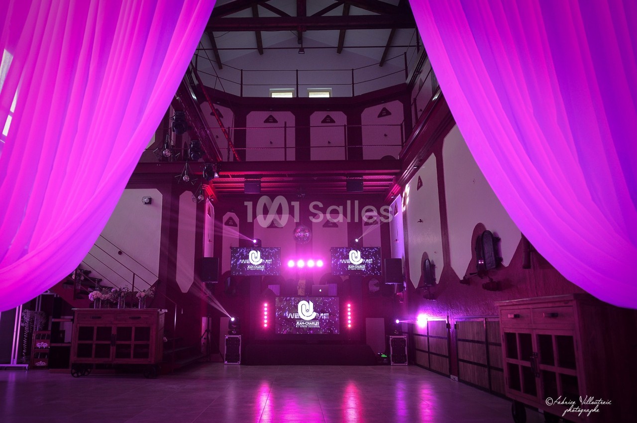 Salle de réception avec éclairage rose, rideaux ouverts au premier plan et écrans lumineux au fond.