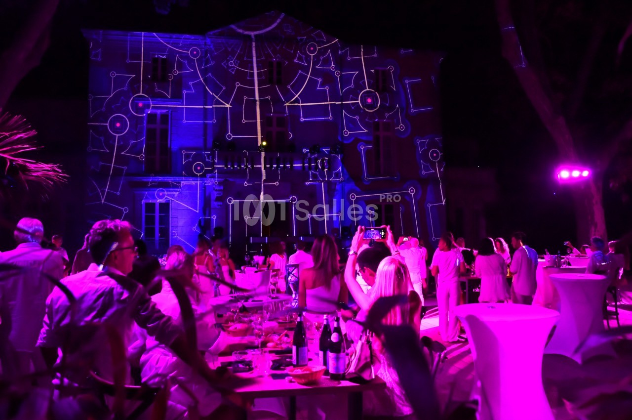 Des invités profitent d'une soirée en plein air avec des projections lumineuses sur la façade d'un bâtiment.