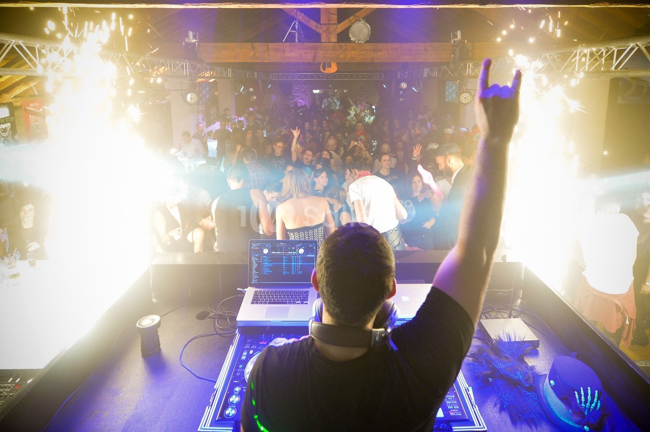 Un DJ anime une soirée en boîte de nuit, face à une foule dansante et des effets lumineux spectaculaires.