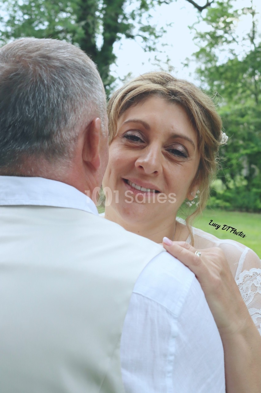 Une femme souriante regarde un homme de dos, dans un cadre extérieur verdoyant.