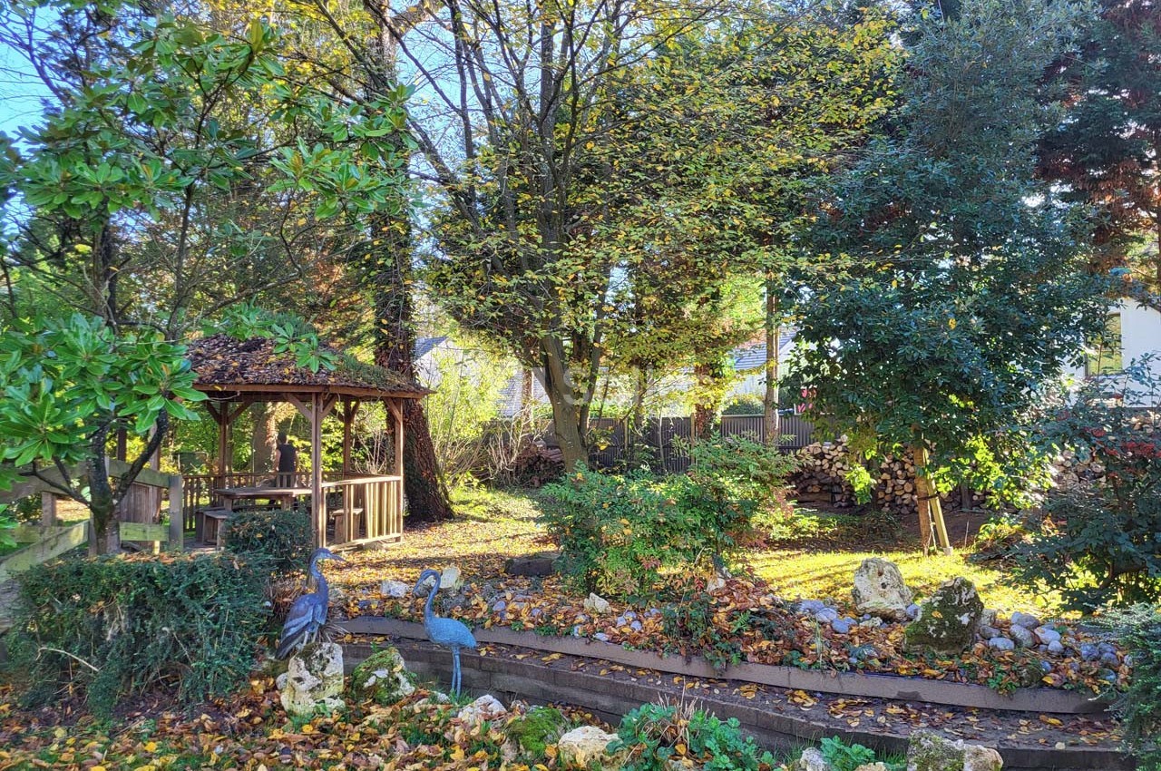 Jardin arboré en automne avec une tonnelle en bois, des statues d'oiseaux et un parterre couvert de feuilles.