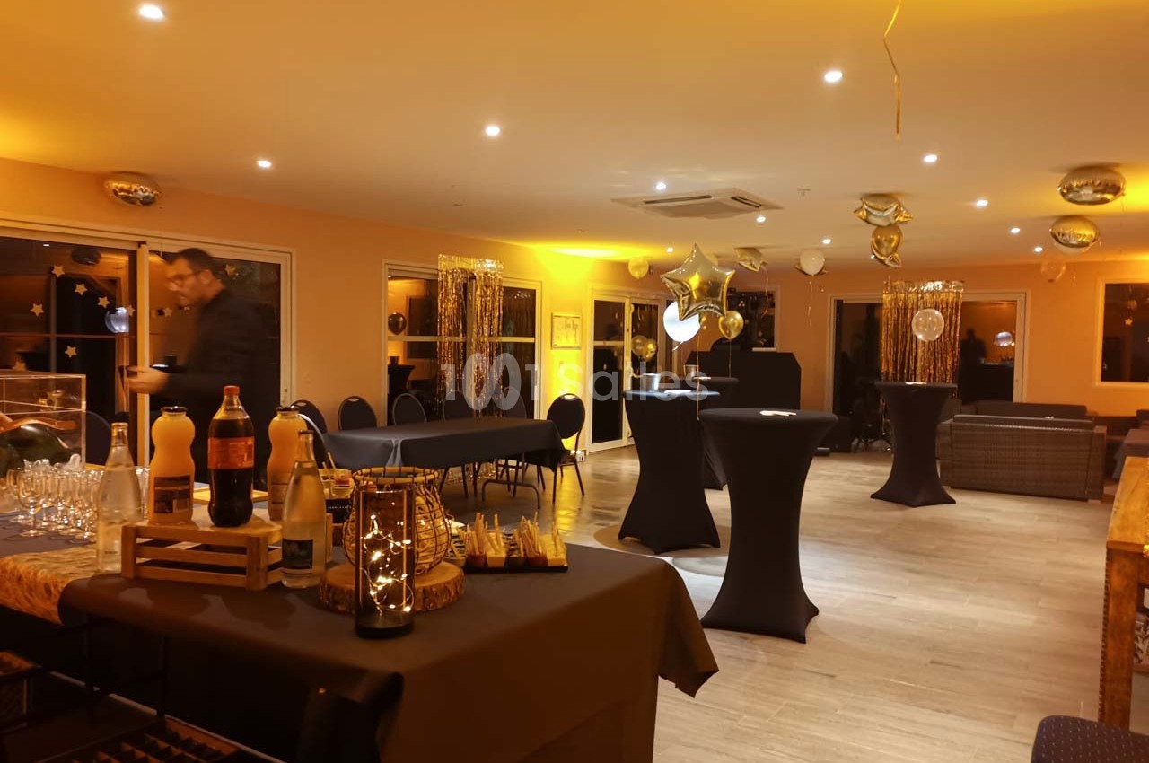Salle décorée pour un événement avec tables hautes, ballons dorés et buffet disposé sur une table.