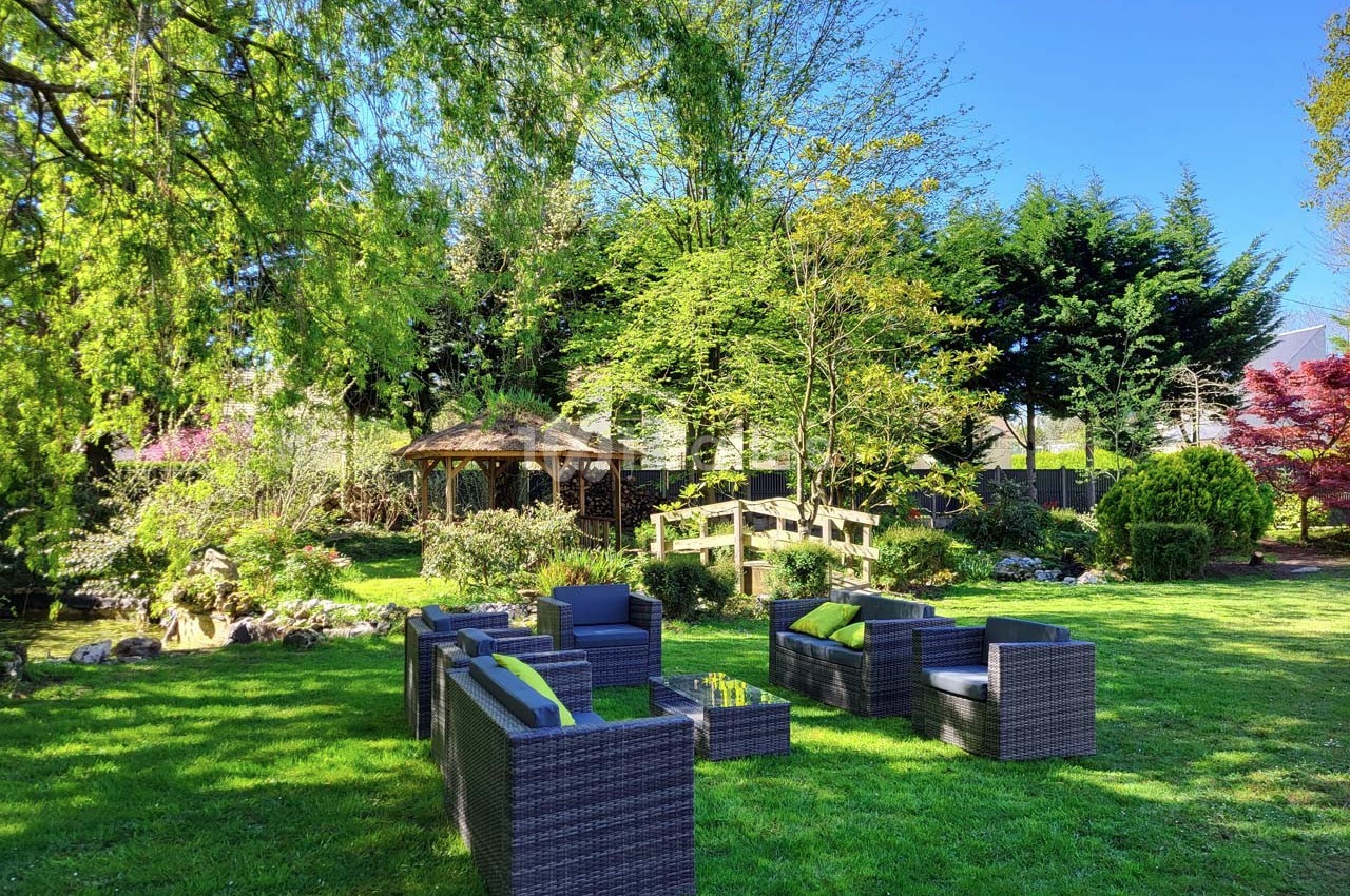 Mobilier de jardin en rotin disposé sur une pelouse verdoyante, entouré d'arbres et d'un kiosque en arrière-plan.