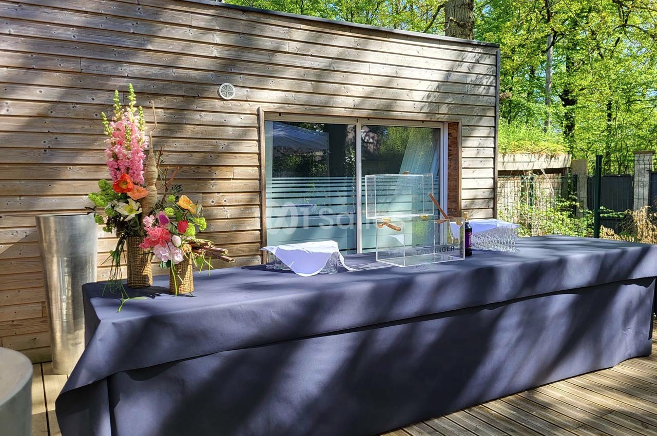 Table drapée de tissu bleu avec des décorations florales et une boîte transparente, située sur une terrasse en bois.