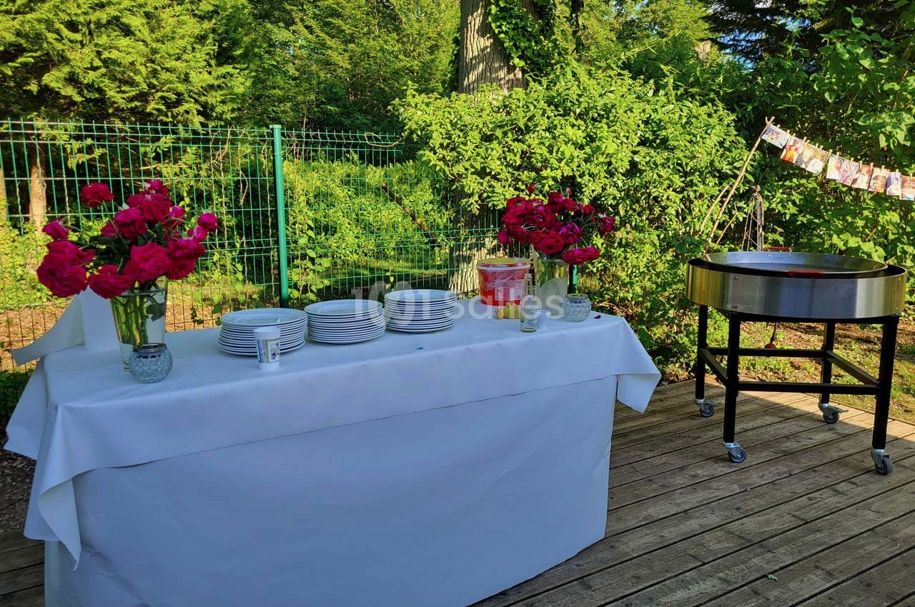 Table dressée en extérieur avec vaisselle blanche, bouquets de fleurs rouges et un barbecue à proximité.