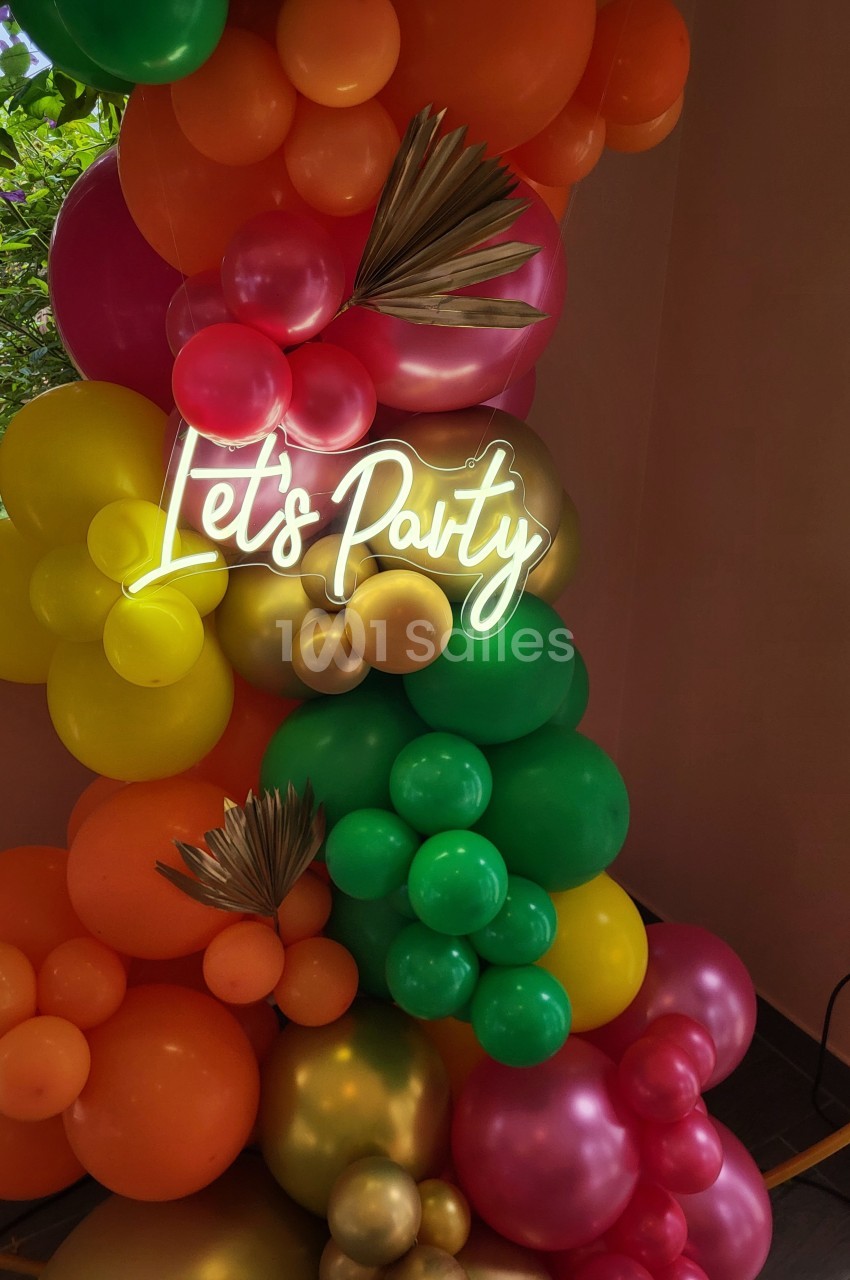 Décoration festive avec des ballons colorés et un néon ’Let's Party’ sur un fond intérieur.