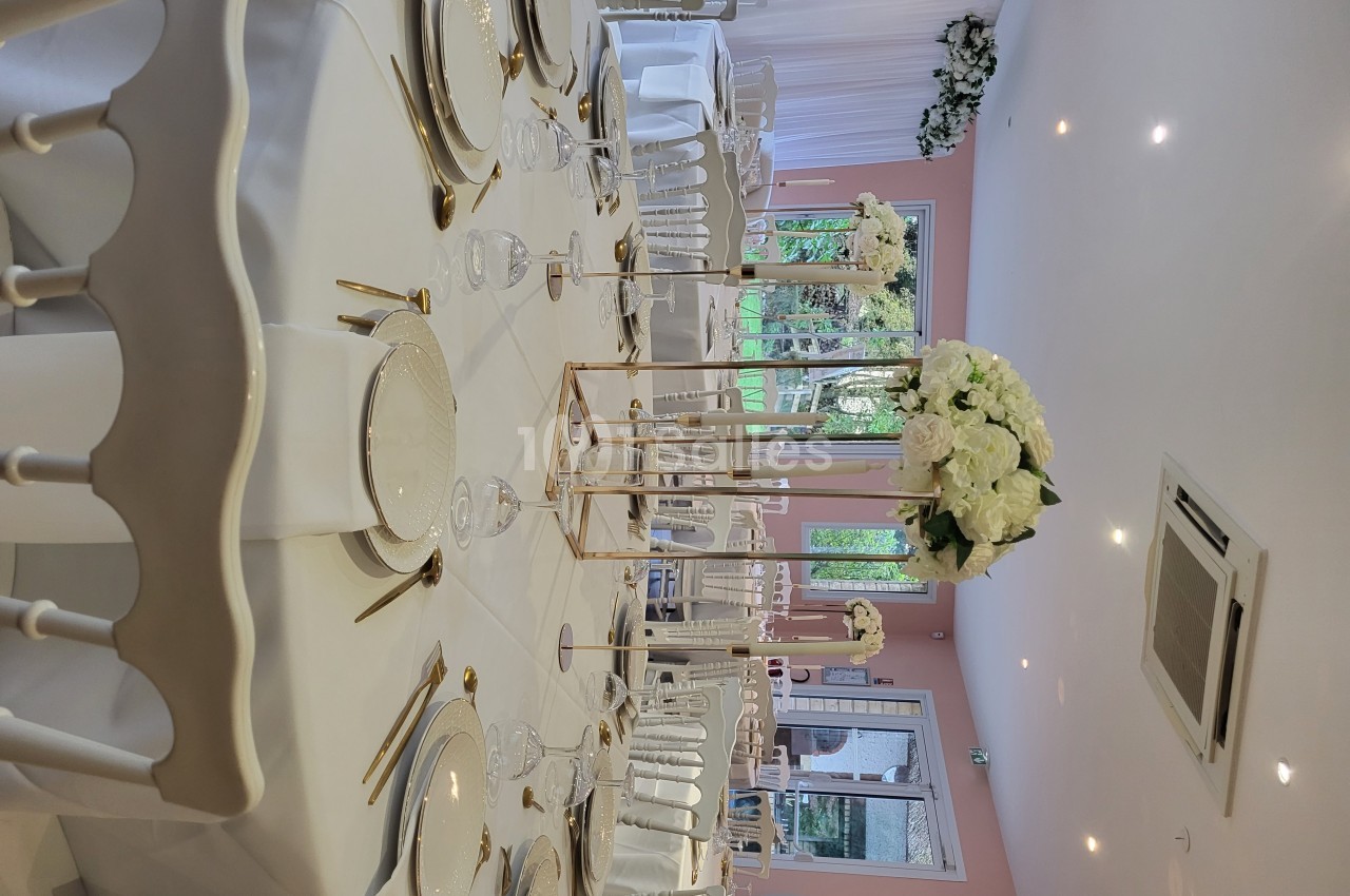 Salle de réception décorée avec des tables rondes, nappes blanches, vaisselle élégante et centres de table fleuris.
